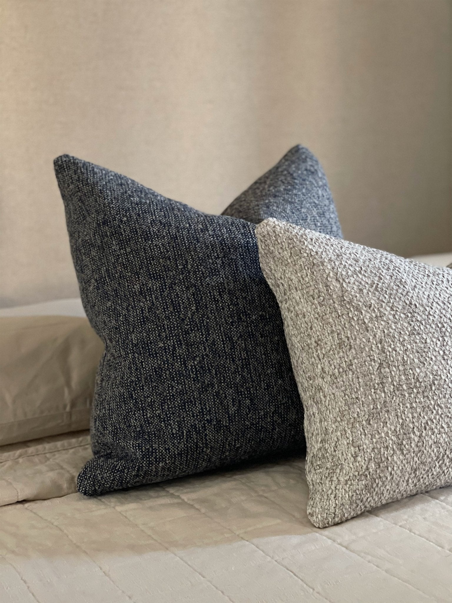 Boucle pillow set in dark blue and taupe featured on cream bedding in minimalist style.