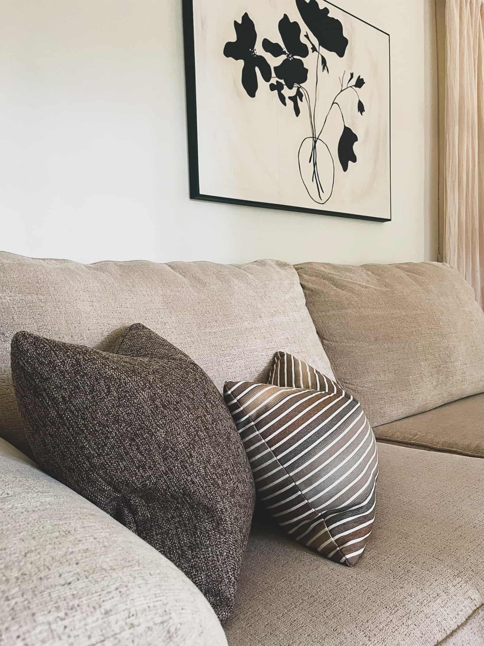 A set of throw pillows in brown earthy tones are placed on cream sofa and styled with minimalist decor