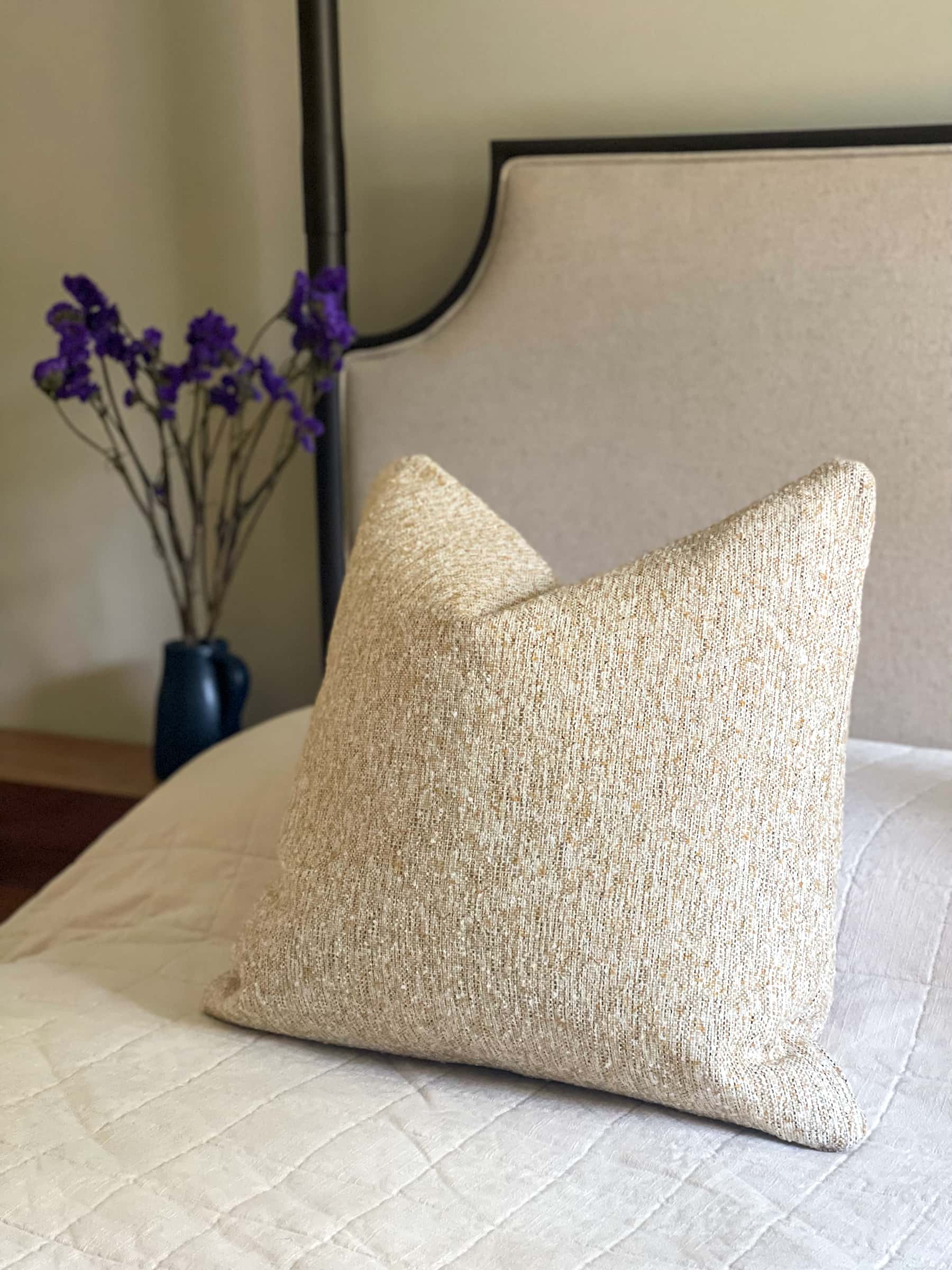 Boucle square pillow in pale yellow and thick fabric sitting in front of a black ceramic vase with delicate deep purple flowers