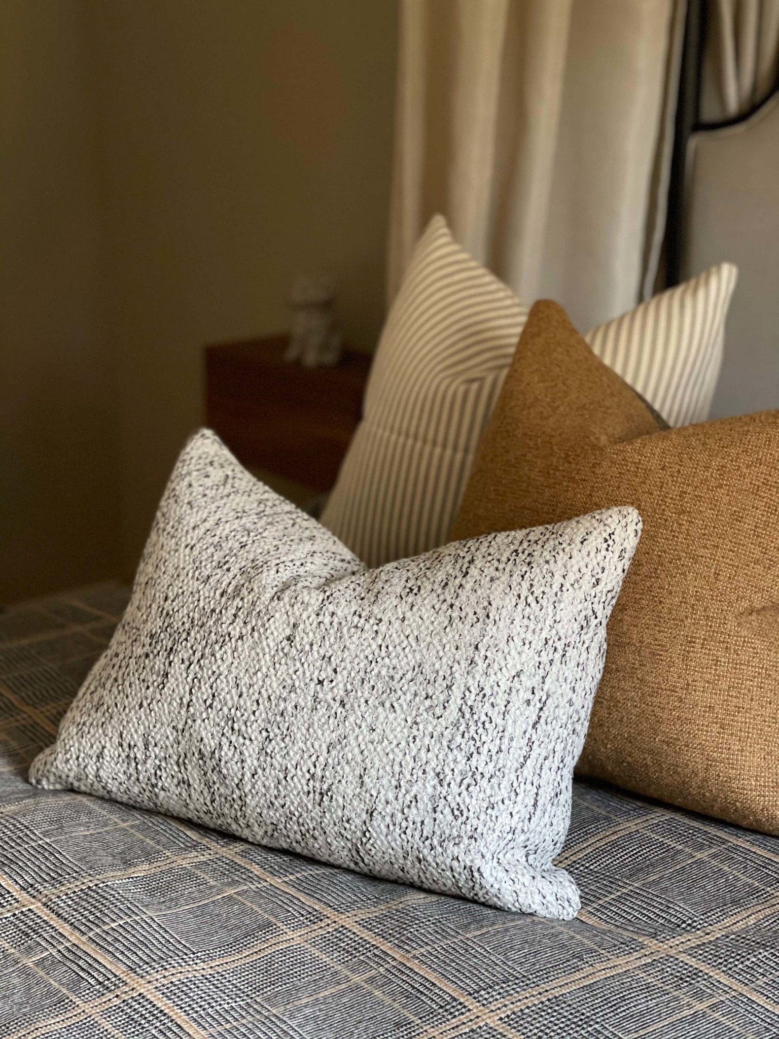 Neutral pillow set for bed featuring a cream boucle lumbar pillow, a tan boucle square pillow, and a beige ticking striped pillow.