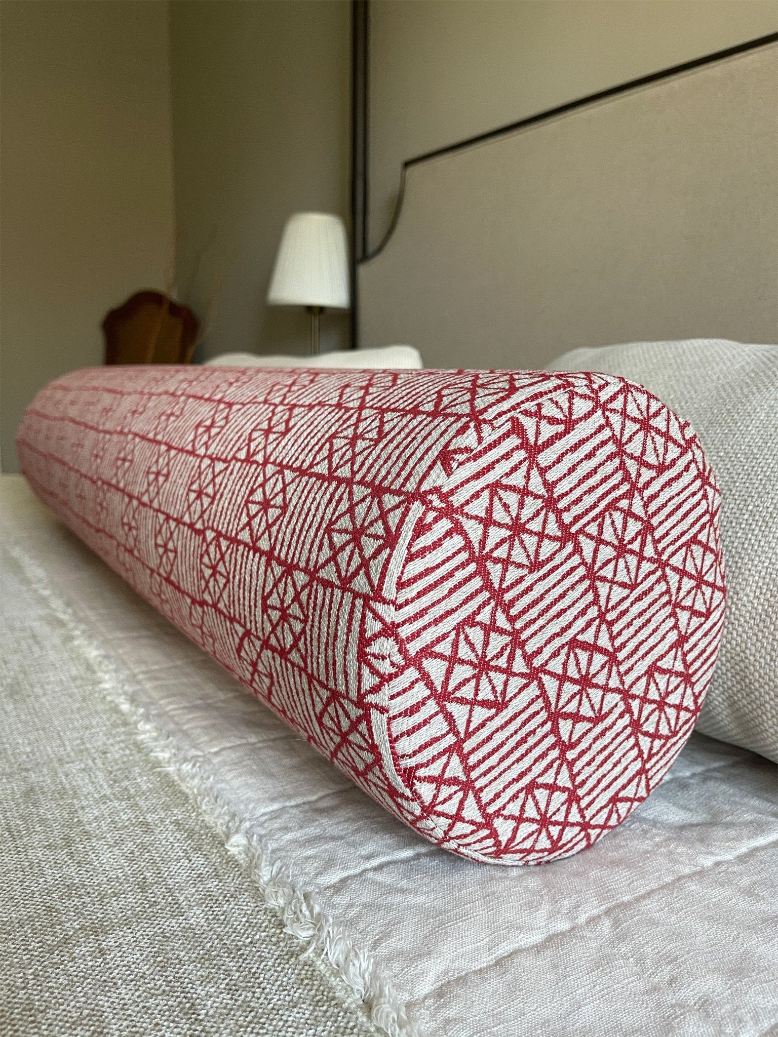 A close-up view of red geometric bolster pillow with firm foam insert add a pop of color on neutral bed