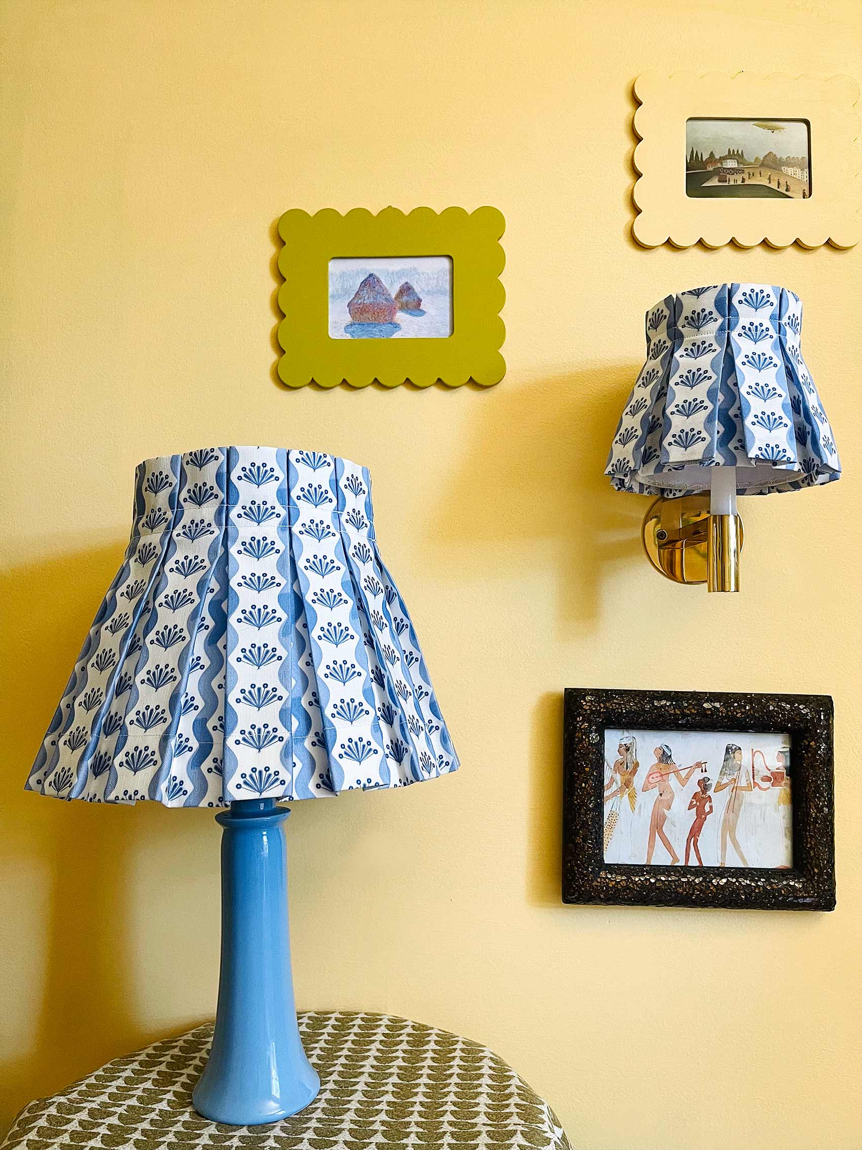 Two blue lamps with patterned shades on a yellow wall with framed pictures.