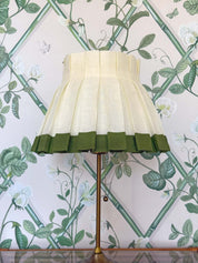 Ivory linen and forest green trimmed lampshade on a brass lampstand set on a dining table in front of a green botanical bamboo wallpaper