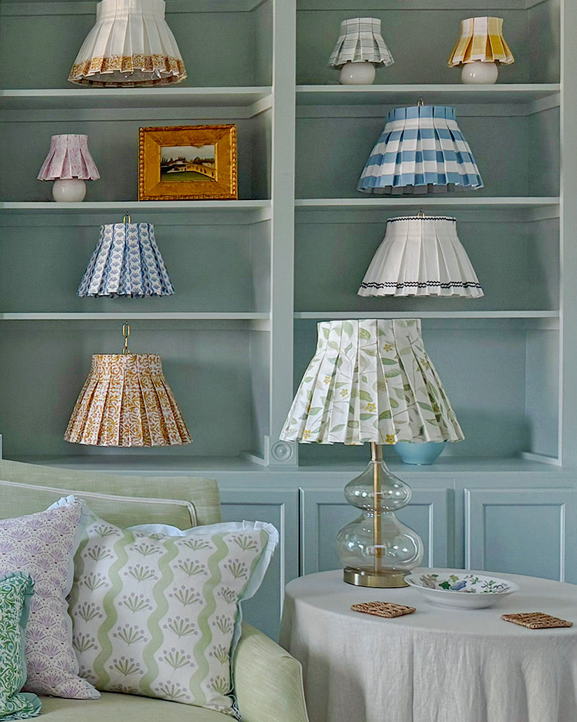 Shelves with various lampshades and a sofa with patterned cushions in a room.