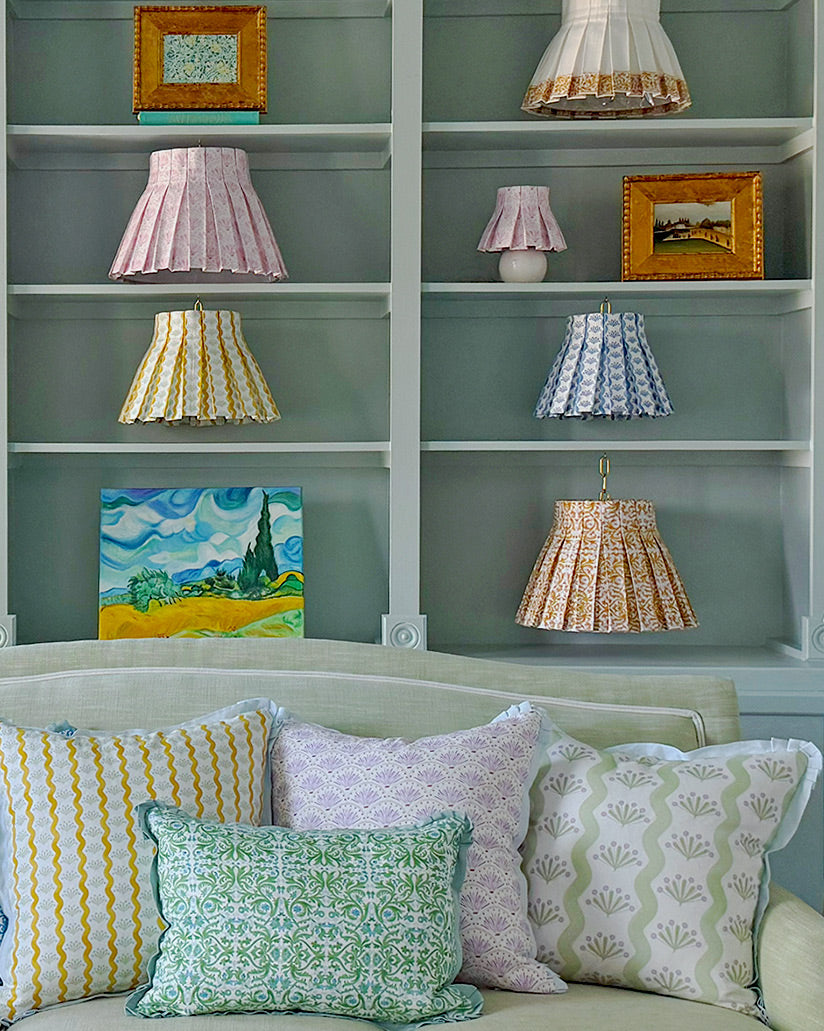 Decorative pillows and lampshades on a sofa with a shelf in the background.