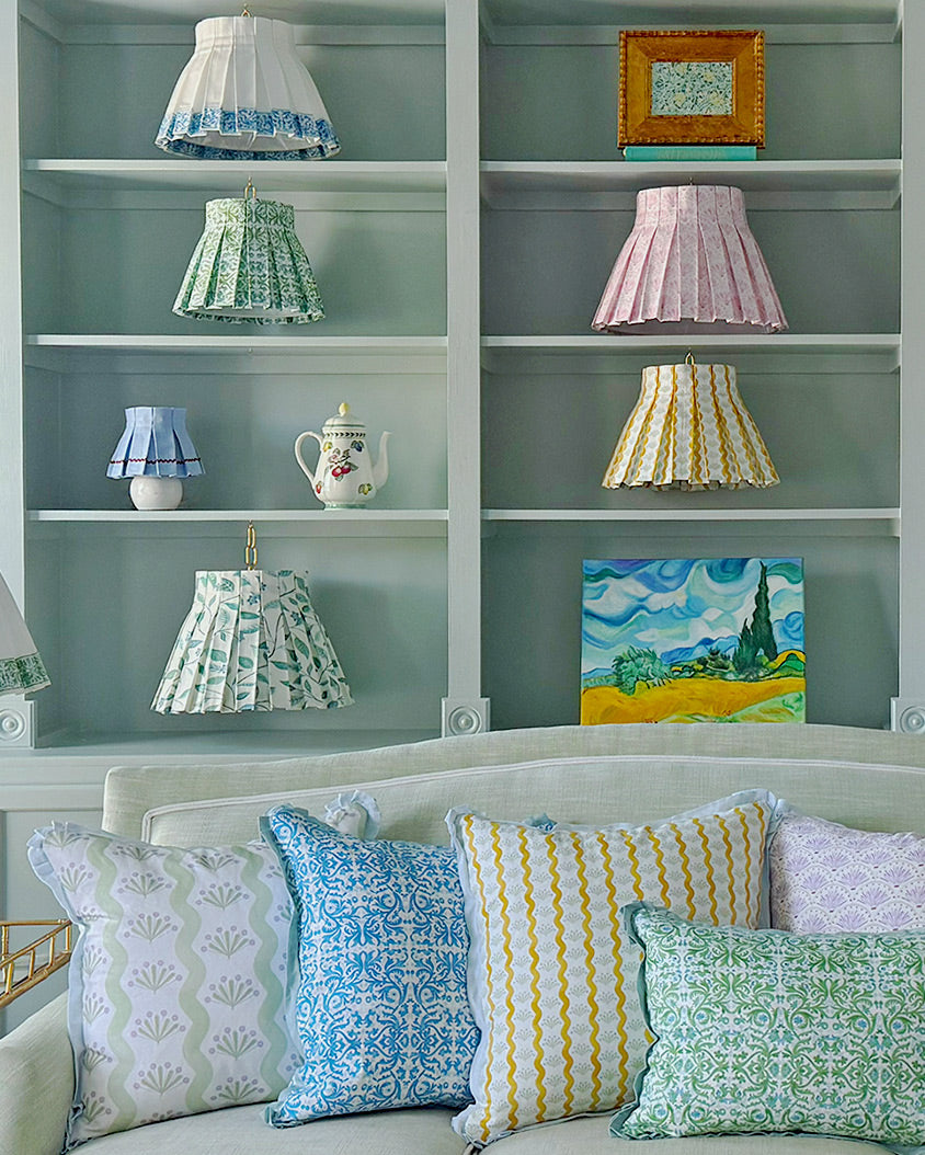 Decorative pillows on a sofa with shelves displaying small lampshades and a teapot.