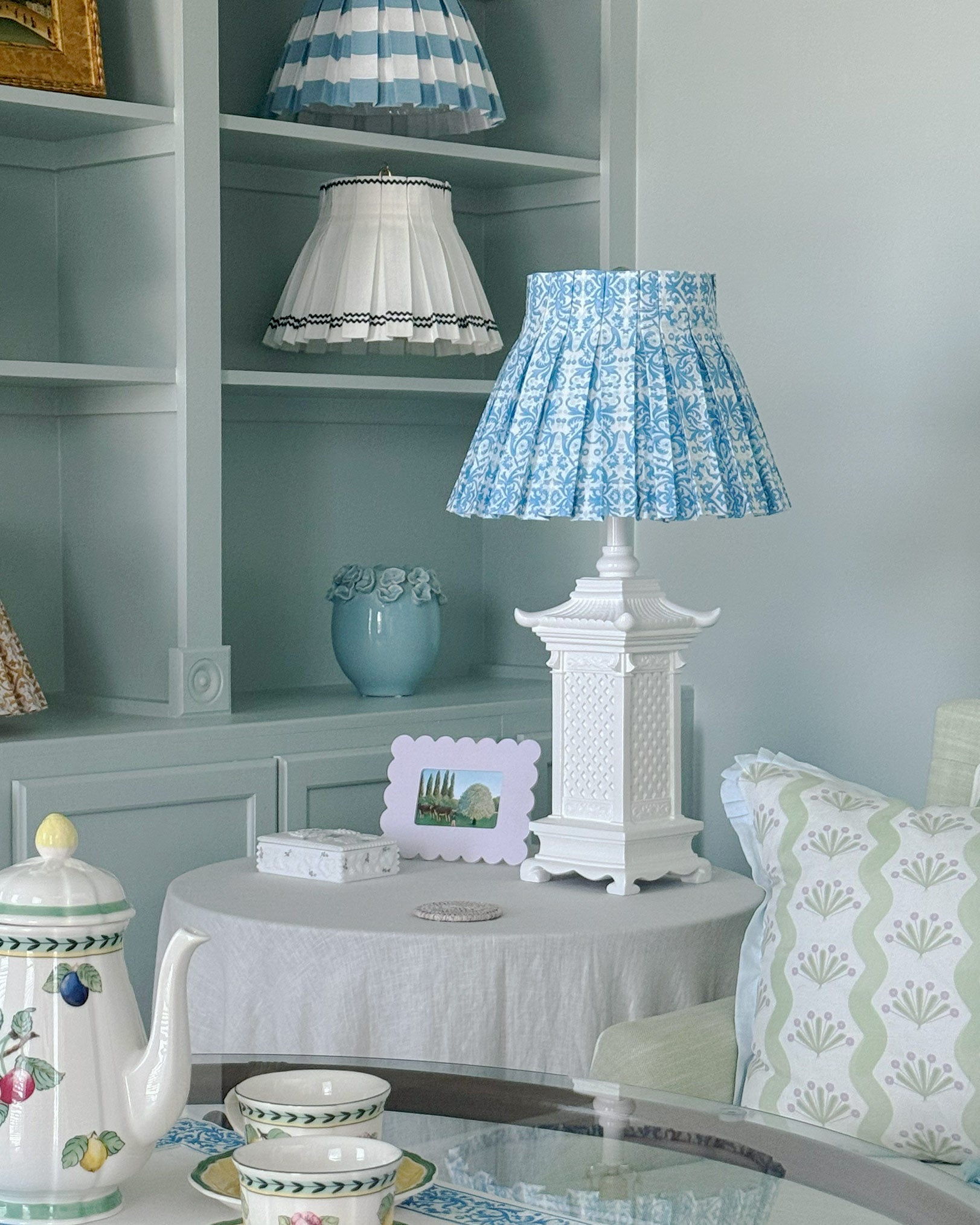 Decorative lamp with blue fresco patterned shade on a table in a room with shelves and decor.