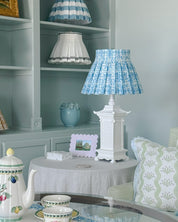 Decorative lamp with blue fresco patterned shade on a table in a room with shelves and decor.